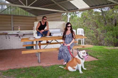 a woman and a man sitting at a picnic table with a dog at Emu Beach Chalets in Albany
