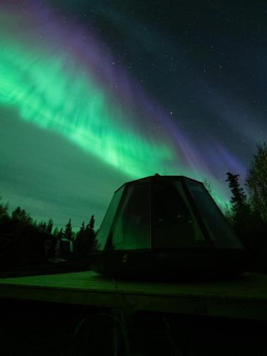 a tent under the northern lights in the sky at Aurora River Camp Glass igloos & cabins in Kiruna