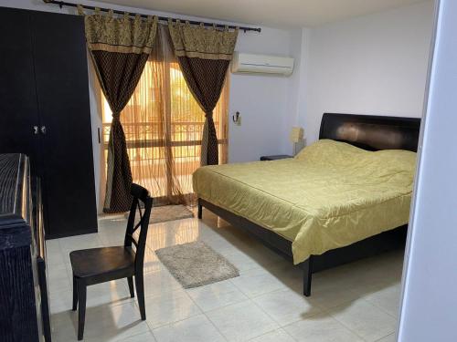 1 dormitorio con 1 cama, 1 silla y 1 ventana en شقة فندقية بإطلالة خيالية مكيفة بالكامل للايجار في مدينتي-Madīnat, en Madinaty