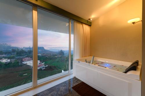 um quarto com uma banheira e uma grande janela em Clouds Nest By Aanvis Inn em Ooty