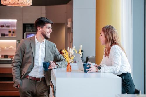 a man and a woman standing at a desk with a laptop at Novotel Suites Luxembourg in Luxembourg