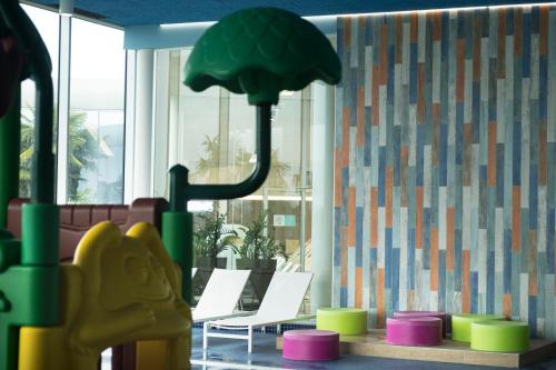 a room with a playground with chairs and a tree at Mjus Resort & Thermal Park in Körmend