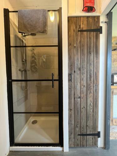 ducha con puerta de cristal junto a la bañera en Shepherds Huts, en Kidlington