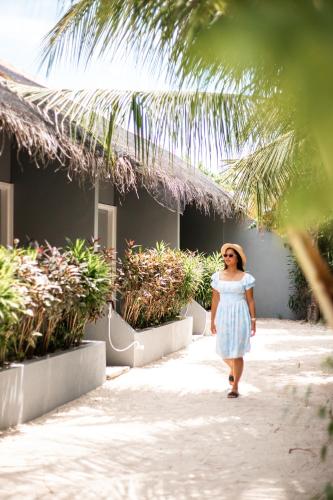 a woman in a blue dress walking down a sidewalk at Tropical Tree in Fehendhoo