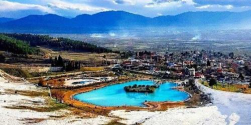 une piscine d'eau bleue avec une ville en arrière-plan dans l'établissement Pamukkale Apollon Garden, à Denizli