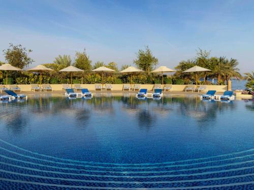 a large swimming pool with chairs and umbrellas at Mövenpick Resort & Spa Tala Bay Aqaba in Aqaba