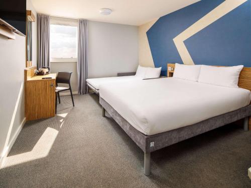 a hotel room with a large bed and a desk at ibis budget London Heathrow Central in Hounslow