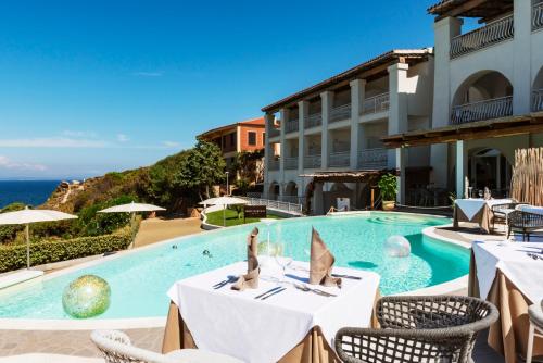 a pool at a hotel with tables and chairs and the ocean at Hotel Moresco in Santa Teresa Gallura