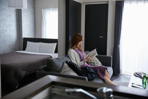 a woman sitting on a couch reading a book in a hotel room at PINN-N4E2Ⅰ in Sapporo