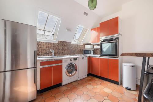 une cuisine avec des armoires orange et un lave-linge/sèche-linge dans l'établissement Renaissance, à Paris