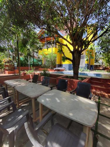 two picnic tables and chairs with a tree in the background at Redstone House by Oxystays Hospitality in Ganpatipule