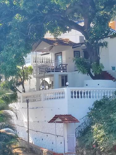 a white house with a balcony and a tree at WhiteHouse Homestay by Oxystays Hospitality in Alibaug