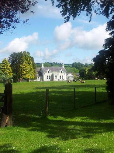 a white house in a field with a fence at Brookhall Cottages in Lisburn