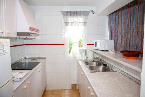 a white kitchen with a sink and a window at Atalaya Bosque Apartamentos in Paguera