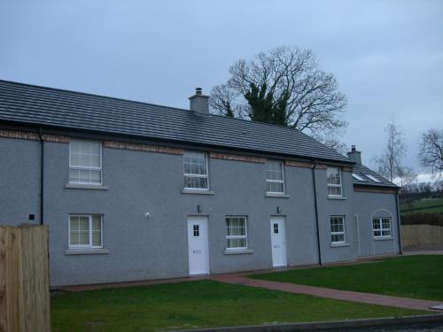 a gray brick house with white doors and a yard at Templemoyle Farm Cottages in Campsey