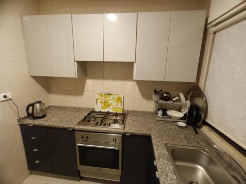 a kitchen with white cabinets and a stove and a sink at Rimini Furnished Apart. in Amman