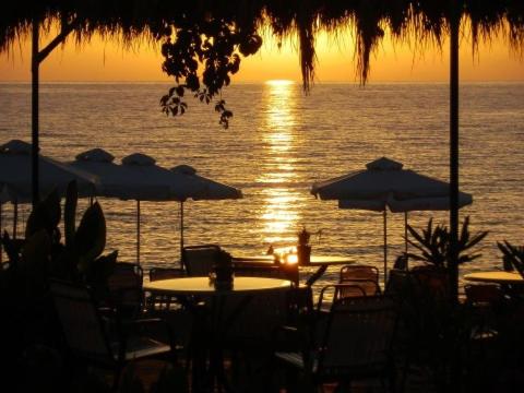 a sunset over the ocean with tables and umbrellas at Dimitra in Petra