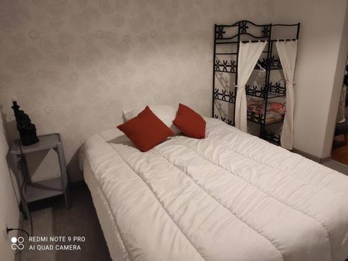 ein großes weißes Bett mit zwei roten Kissen darauf in der Unterkunft Haut de villa : véranda, terrasse, vue piscine in Thiviers