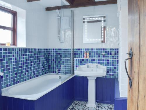 a blue tiled bathroom with a tub and a sink at Heathcote Cottage in Hickling