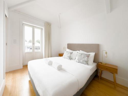 a white bedroom with a large white bed and a window at Vibrant Host -Bonfim in Porto