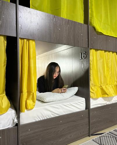 a woman sitting in a bunk bed looking at her cell phone at Crypto Hostel in Almaty