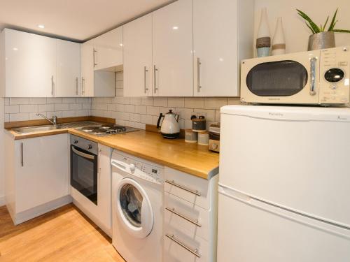 a kitchen with white cabinets and a washer and dryer at The Pool House in Tywardreath