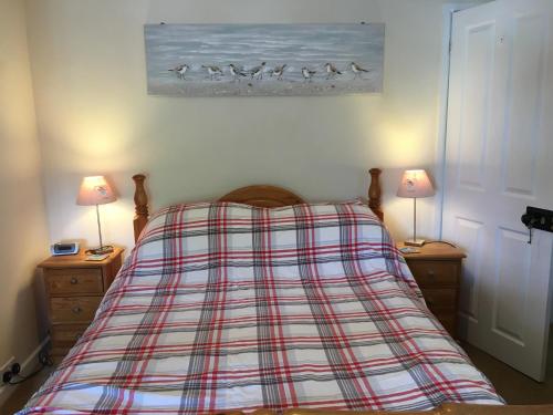 een slaapkamer met een bed met een geruite deken en 2 lampen bij Millstones in Chideock