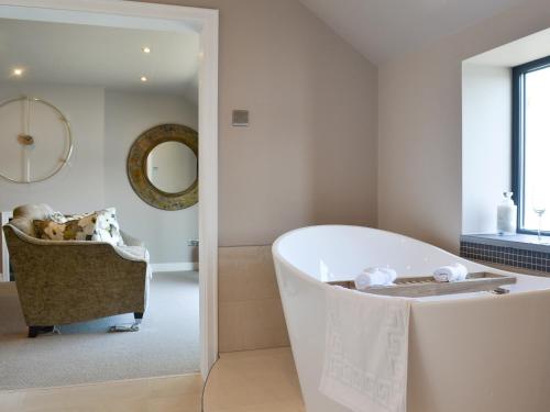 a white bathroom with a tub and a chair at Tan Y Fford in Bangor