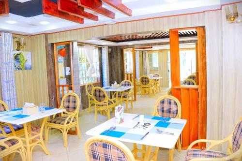 a restaurant with white tables and chairs and windows at Ohm Village Inn(OVI) in Kitui