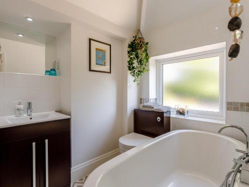 a bathroom with a tub and a toilet and a window at Yew Tree House in Chideock