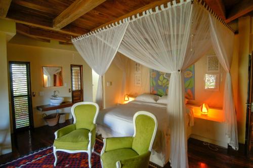 a bedroom with a canopy bed with two green chairs at Ebony beach in Vilanculos