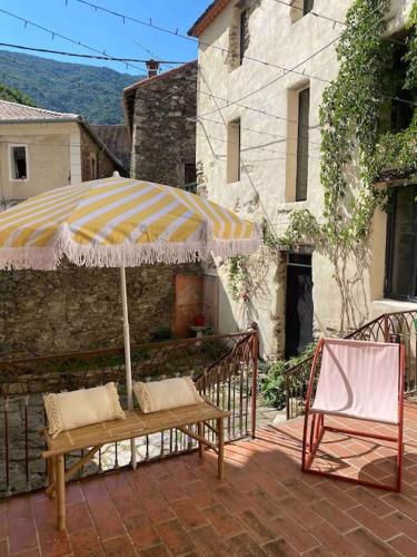 a patio with a bench and an umbrella and a chair at Appartement de Charme dans un Ancien Mas Cévenol piscine et jacuzzi in Valleraugue