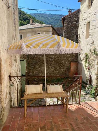a bench sitting under an umbrella on a patio at Appartement de Charme dans un Ancien Mas Cévenol piscine et jacuzzi in Valleraugue
