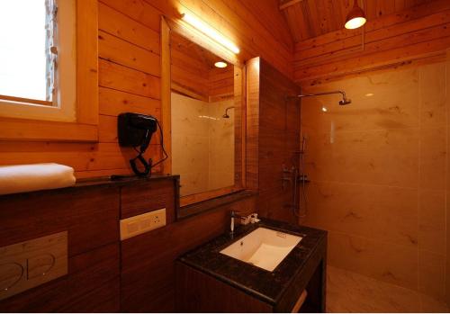 a bathroom with a sink and a shower in a cabin at Antaraal Resort & Spa A Village Resort in Dharamshala
