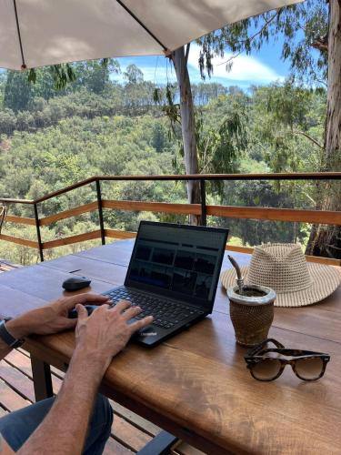 a man using a laptop computer on a wooden table at Complejo de Cabañas Eco-sustentables - La escondida - in San Salvador de Jujuy