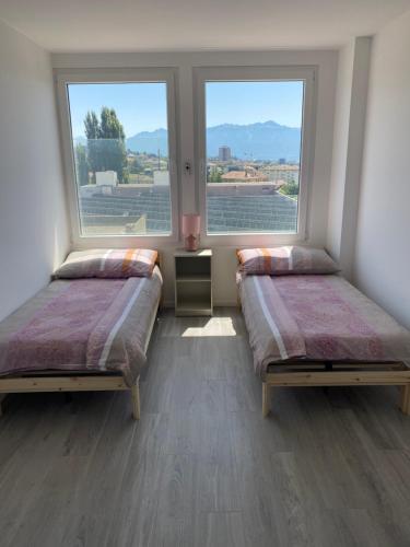 two beds in a room with two windows at Charmant appartement près de EPFL UNIL Lausanne in Renens