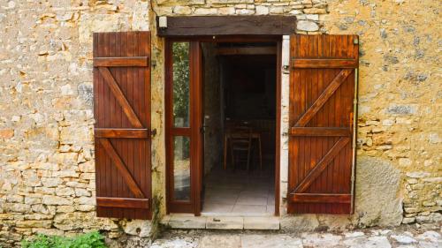 una puerta abierta de un edificio de piedra con puertas de madera en Le nid dans la maison, en Cubjac