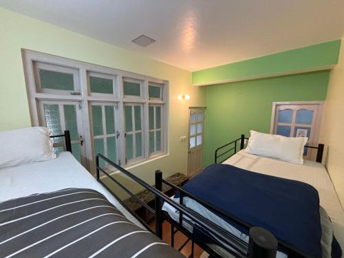 two beds in a room with green walls and windows at Zu-Zu Hostels in Shimla