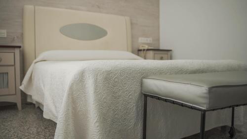 a bedroom with a white bed and a stool at Hotel Restaurante Boabdil in Otura