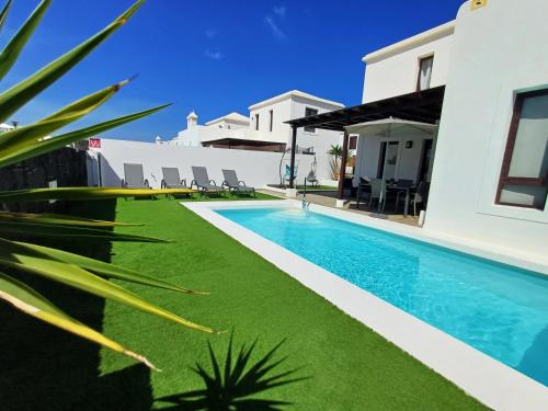 a swimming pool with green grass next to a house at Casa Sunny in Yaiza