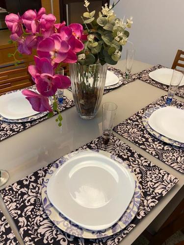 a table with plates and a vase of flowers on it at APARTAMENTO SOL E MAR VITÓRIA in Vitória