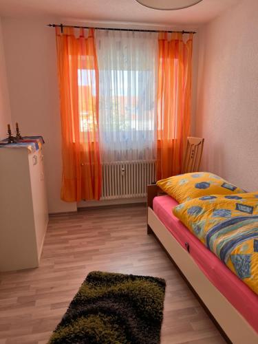 Schlafzimmer mit einem Bett und einem Fenster mit orangefarbenen Vorhängen in der Unterkunft Premium Handwerker- & Monteurzimmer mit Gemeinschaftsbad in Rosenfeld