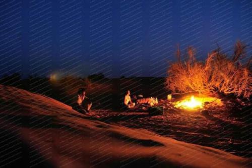 two people sitting around a fire in the sand at night at Private Camp25km-from DOUZ in Douz