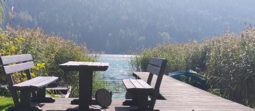 a picnic table and two benches on a wooden pier overlooking a lake at Haus Birke in Weissensee