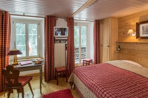 a bedroom with a bed and a desk and windows at Historic Hotel du Pillon in Les Diablerets