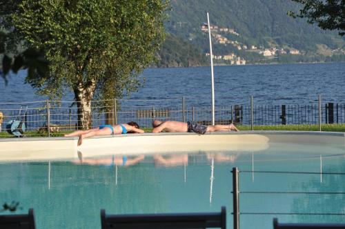 two people laying on the edge of a swimming pool at Tullio Hotel in Gravedona