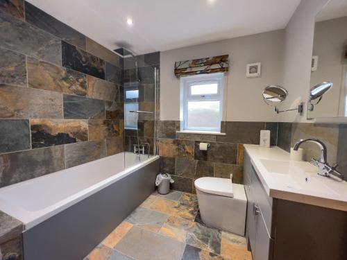 a bathroom with a tub and a toilet and a sink at Lake View luxury home with Lake Ullswater view & 2 ground floor bedrooms ideal for 2 families in Watermillock