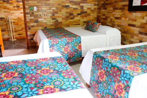 Habitación con 2 camas y 2 mesas con mantas de colores. en Hotel Chalet San Juan de Ticlan, en Armenia