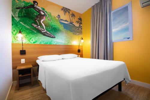 a bedroom with a bed and a painting of a surfer at Hotel Dan Inn São Carlos in São Carlos