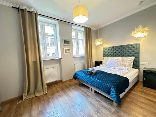 a bedroom with a bed with a blue comforter and two windows at Starovka Apartament in Elblag